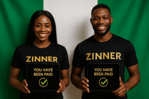 Male And Female Zinn Hub Marketplace Nigerian Freelancers Wearing Black &Quot;Zinner&Quot; Shirts Hold Tablets Displaying The Message &Quot;You Have Been Paid&Quot; In Gold With A Green Checkmark, Standing In Front Of The Nigerian Flag.